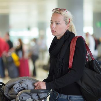 Casual blond young woman using her cell phone while queuing for flight check-in and baggage drop. Wireless network hotspot enabling people to access internet conection. Public transport.