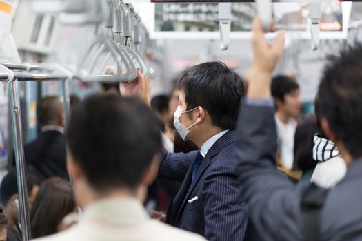 Passengers traveling by Tokyo metro. Business people commuting to work by public transport in rush hour. Shallow depth of field photo. Horizontal composition.