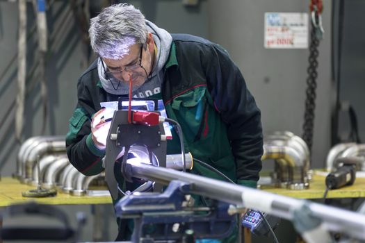 Industrial operator setting  computer controlled process of orbital welding machine in  stainless steel pipes manufacturing workshop.