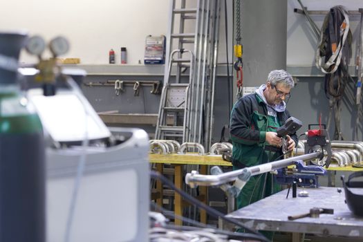 Industrial operator setting  computer controlled process of orbital welding machine in  stainless steel pipes manufacturing workshop.