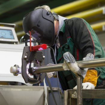 Industrial operator setting  computer controlled process of orbital welding machine in inox pipes manufacturing workshop. Square composition.