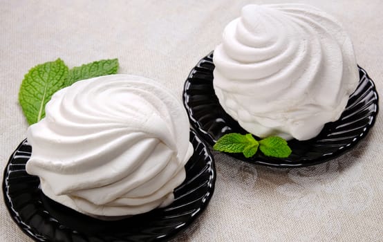 White sweet marshmallow dessert on black saucers with sprigs of fresh mint on linen fabric.