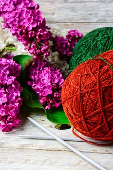 Balls of wool yarn for knitting and branches of lilac blossoms