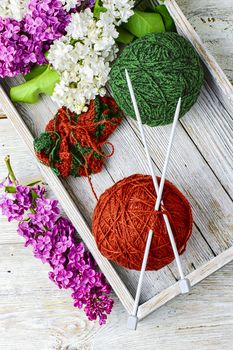 Balls of wool yarn for knitting and branches of lilac blossoms
