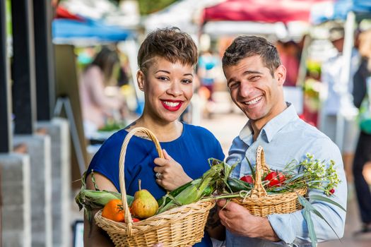 Smiling couple with baskets of produce at farmers market