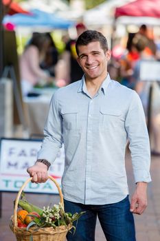 Smiling man with basket of produce at farmers market