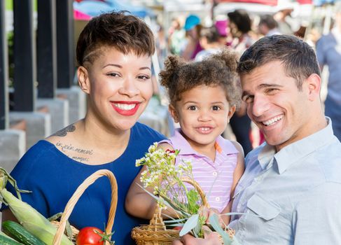 Smiling young family with baskets of produce at farmers market