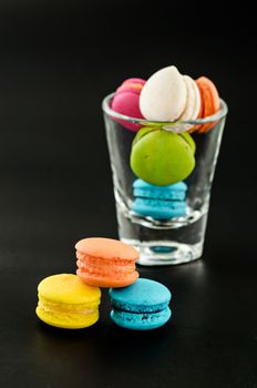 Colorful macarons with glass cup on black background