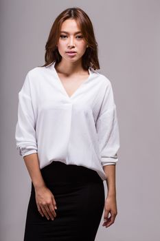 Attractive Asian American businesswoman in white blouse and black skirt looking at camera on gray background