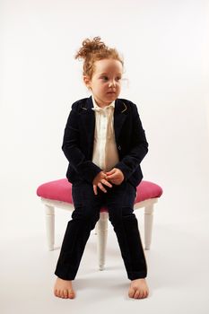 Little girl in black suit sitting on a rose stool