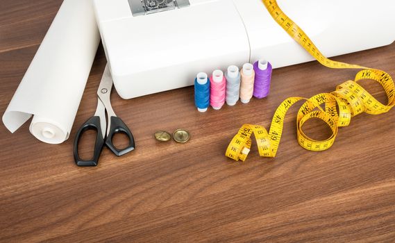 Sewing machine with many sewing utensils on wooden table, closeup