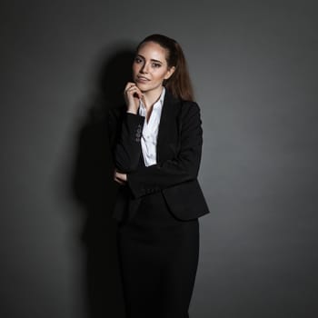Portrait of young businesswoman in black suit on dark background