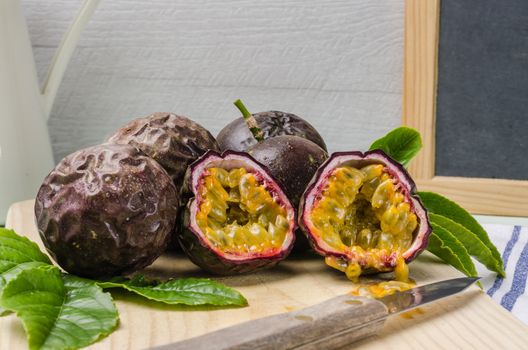 Passion fruits with leaves, knife and white flowers in jar on the vintage wooden table.