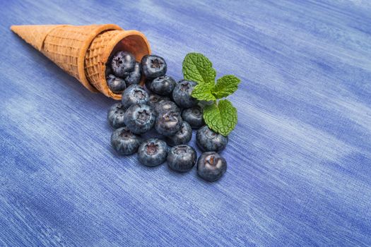Waffle cones with blueberries and mint leaf on rustic textured background. Top view with copy space.