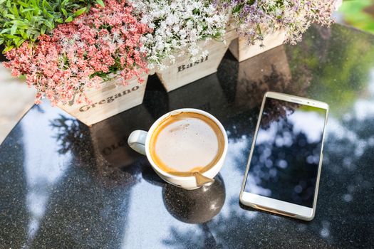 Digital smartphone and cup of coffee on desk with vintage flower. Simple coffee break in morning / selective focus