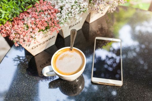 Digital smartphone and cup of coffee on desk with vintage flower. Simple coffee break in morning / selective focus