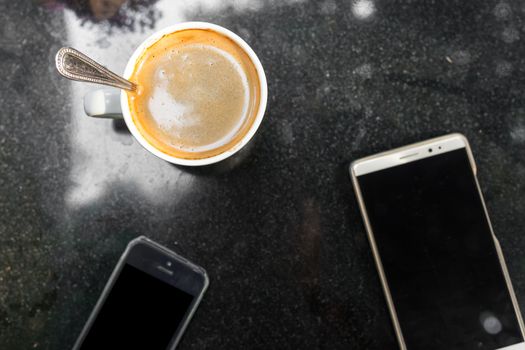 Digital smartphone and cup of coffee on desk with vintage flower. Simple coffee break in morning / selective focus