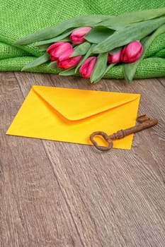 Envelope, rusty key and red tulip on a wooden background