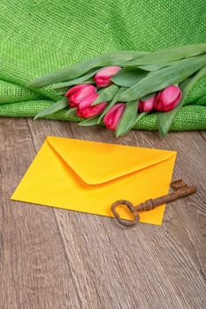 Envelope, rusty key and red tulip on a wooden background