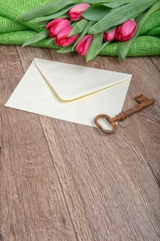 Envelope, rusty key and red tulip on a wooden background