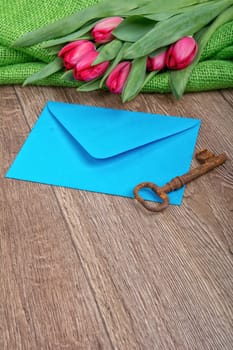 Envelope, rusty key and red tulip on a wooden background