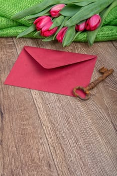 Envelope, rusty key and red tulip on a wooden background