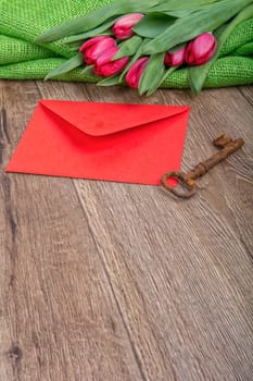 Envelope, rusty key and red tulip on a wooden background