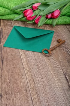 Envelope, rusty key and red tulip on a wooden background