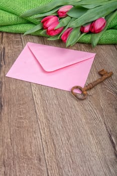 Envelope, rusty key and red tulip on a wooden background