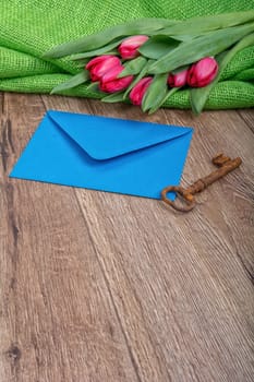 Envelope, rusty key and red tulip on a wooden background