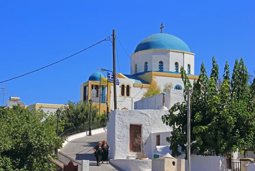 Church in sunday morning sunshine. White walls and blue cupola. Women dressed in black are coming from sunday morning prayer. Lagades village, Kos, Greece.