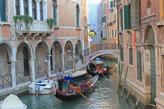 Two gondolas with passengers in canal near the old building with damaged wall.