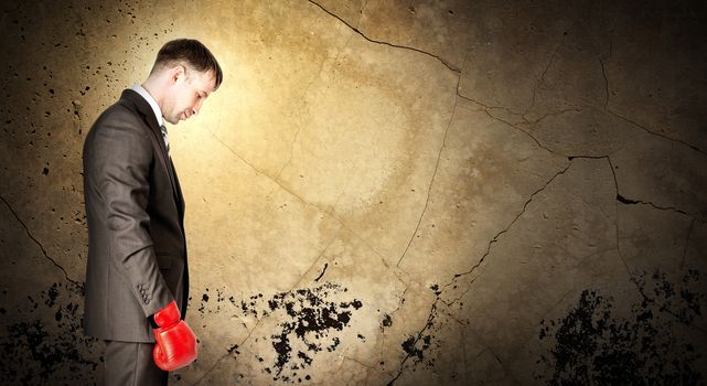 Businessman wearing boxing gloves and looking sad on grey wall background with light