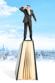 Businessman standing on book and looking away on city background