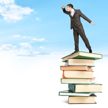 Businessman staying on pile of books on top among clouds and looking into distance