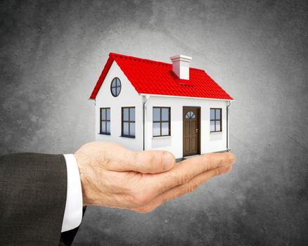 Business man holding model house in hand on grey background