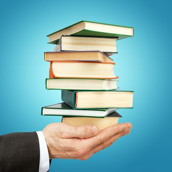 Business man holding stack of books on blue background