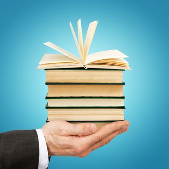 Business man holding stack of books with open one on blue background