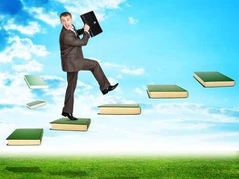 Businessman walking on books in sky with green grass