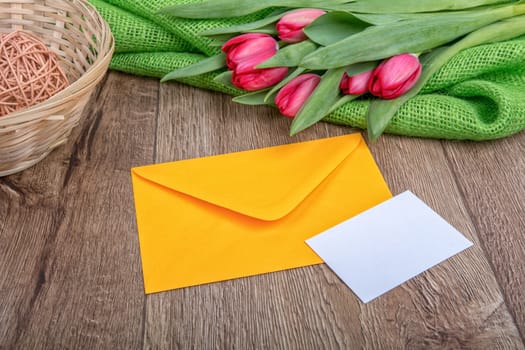 Envelope with sheet of paper and red tulips on a wooden background