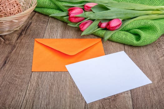 Envelope with sheet of paper and red tulips on a wooden background