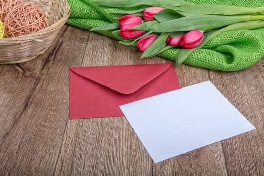 Envelope with sheet of paper and red tulips on a wooden background