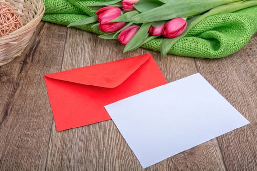 Envelope with sheet of paper and red tulips on a wooden background