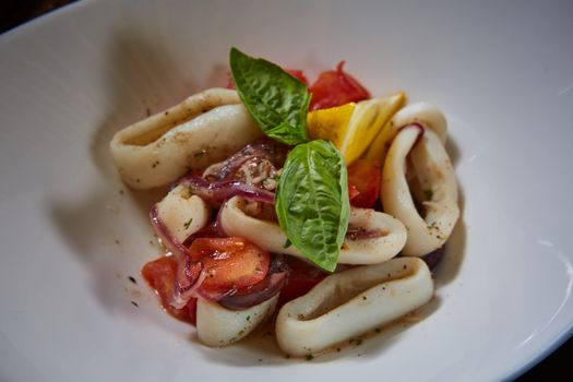 healthy rings squid salad with tomatoes decorated with basil leaves