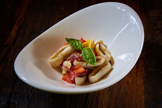 healthy rings squid salad with tomatoes decorated with basil leaves