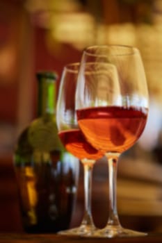 two wine glasses filled with red wine and wine bottle in background. Soft focus