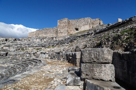 View of Miletus amphitheater in Aydin, Turkey with stone stairs on bright blue sky background.