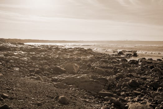 waves break on the black rocks at ballybunion beach in ireland in sepia