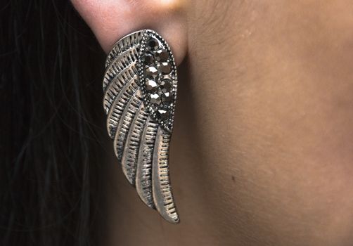 a lady or girl wearing a silver metal wing styled earing up close