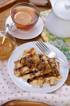 Breakfast pancakes on apples with caramel and chocolate and cup of tea